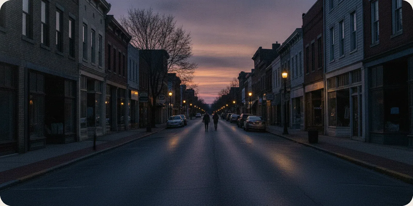 A quiet American main street at dusk with lit office windows above the shopfronts.