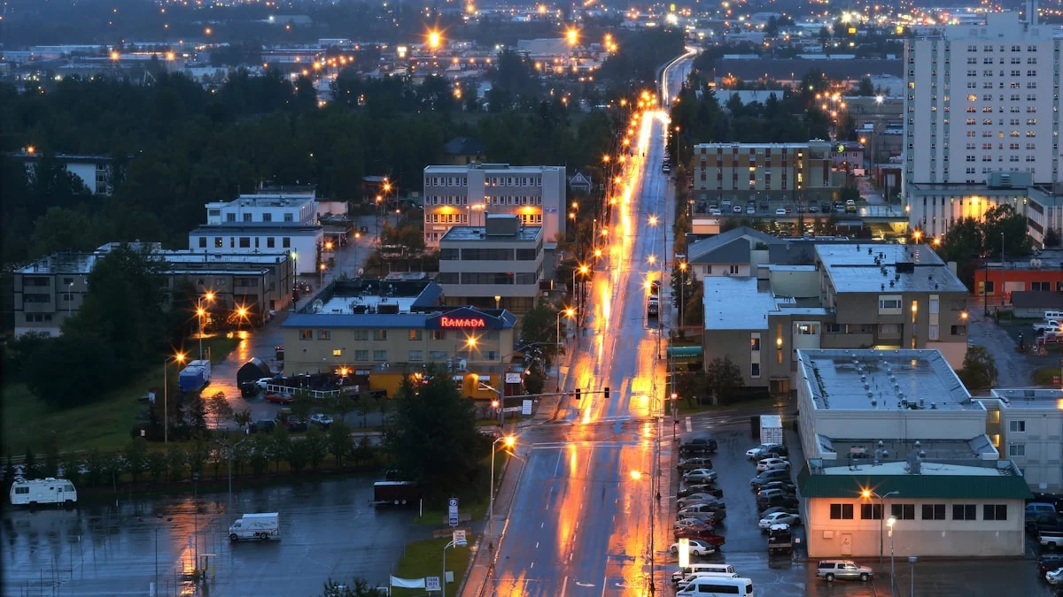 Vehicles on a wet downtown street in Anchorage, Alaska, lit by streetlamps after a winter rain, mid-evening rush.