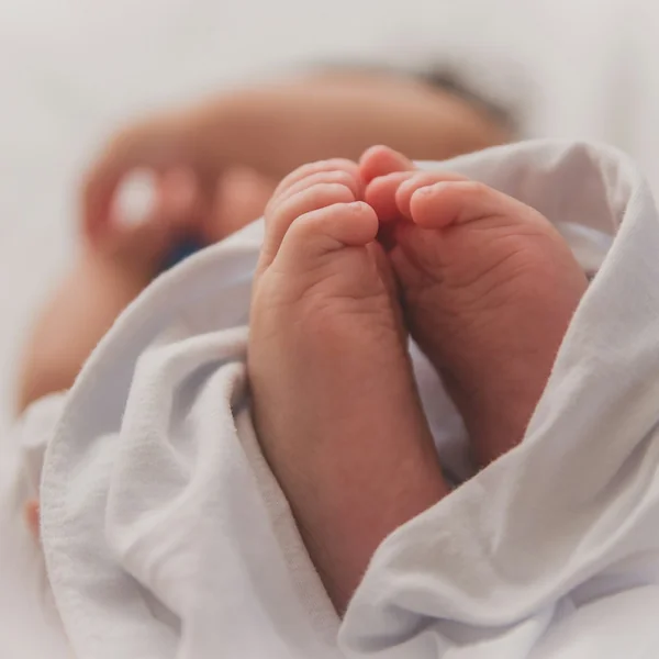 A sleeping newborn's feet wrapped in a soft white blanket.