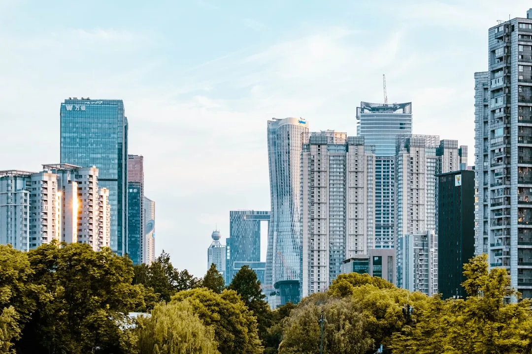 A wide view of a modern Chinese city skyline at dusk, warm office lights visible in glass towers against a deep blue sky.