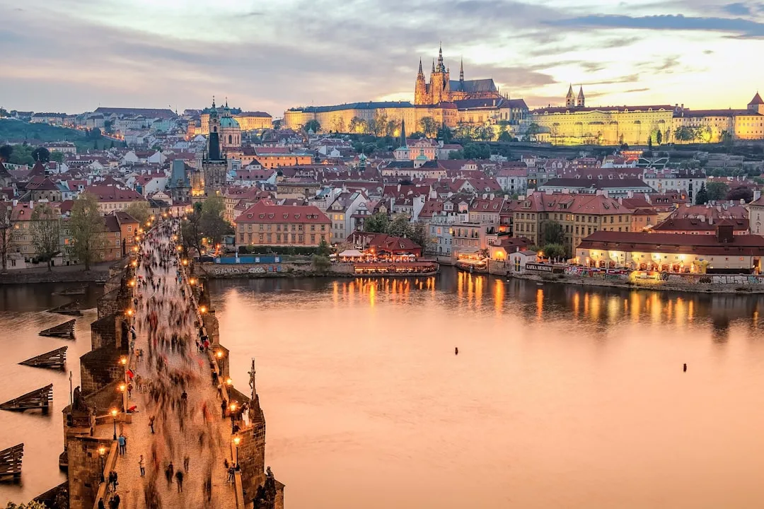 Prague Old Town rooftops and the Vltava river at golden hour with the castle on the hill behind.