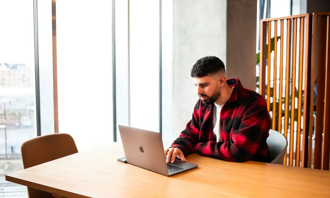 A finance lead reviews a payroll spreadsheet at a bright Copenhagen desk, daylight from a tall window behind.