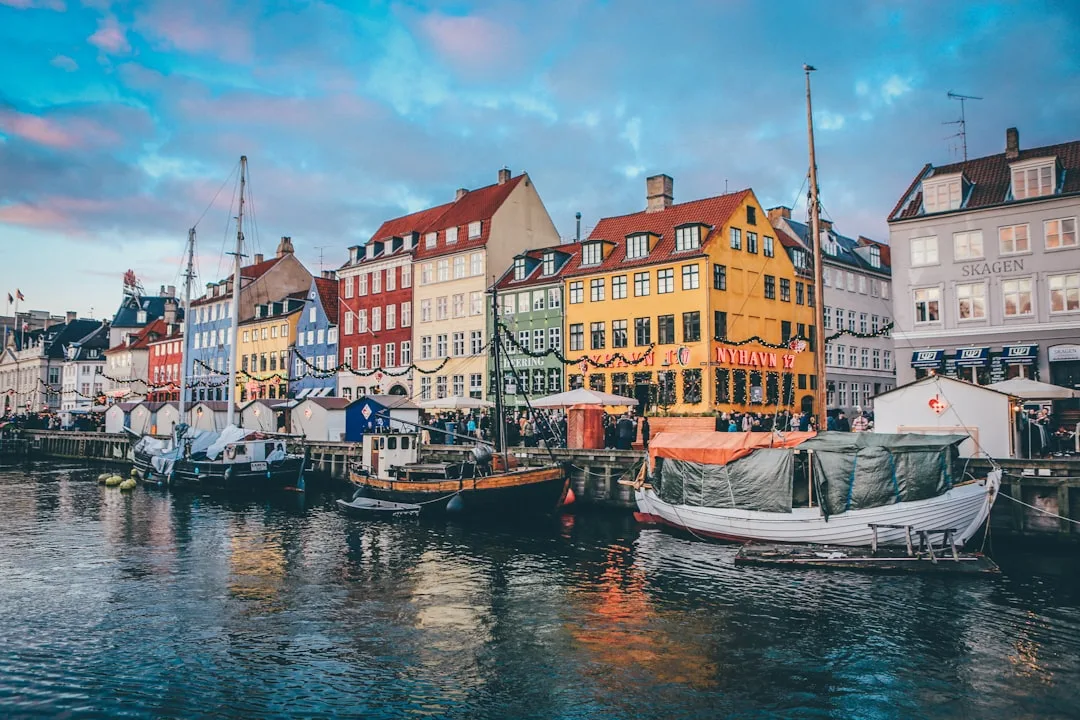 Copenhagen harbour at golden hour with the coloured townhouses of Nyhavn reflected in calm water.