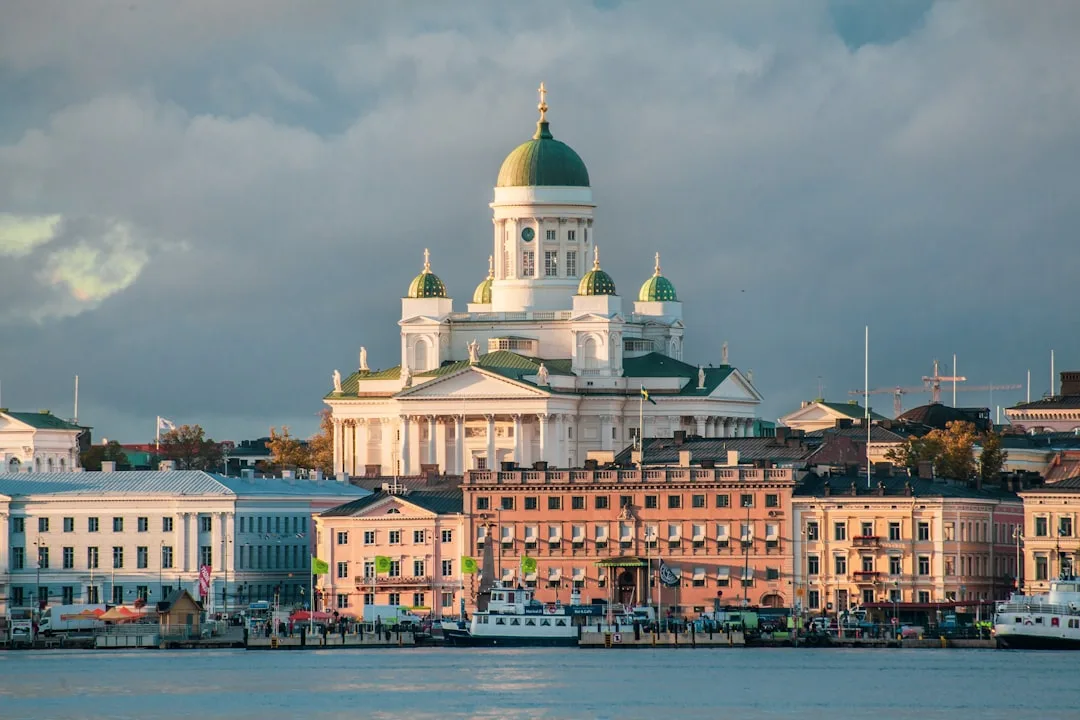 Helsinki harbour at dusk with the white Lutheran Cathedral lit against a soft blue evening sky, viewed from across the market square.