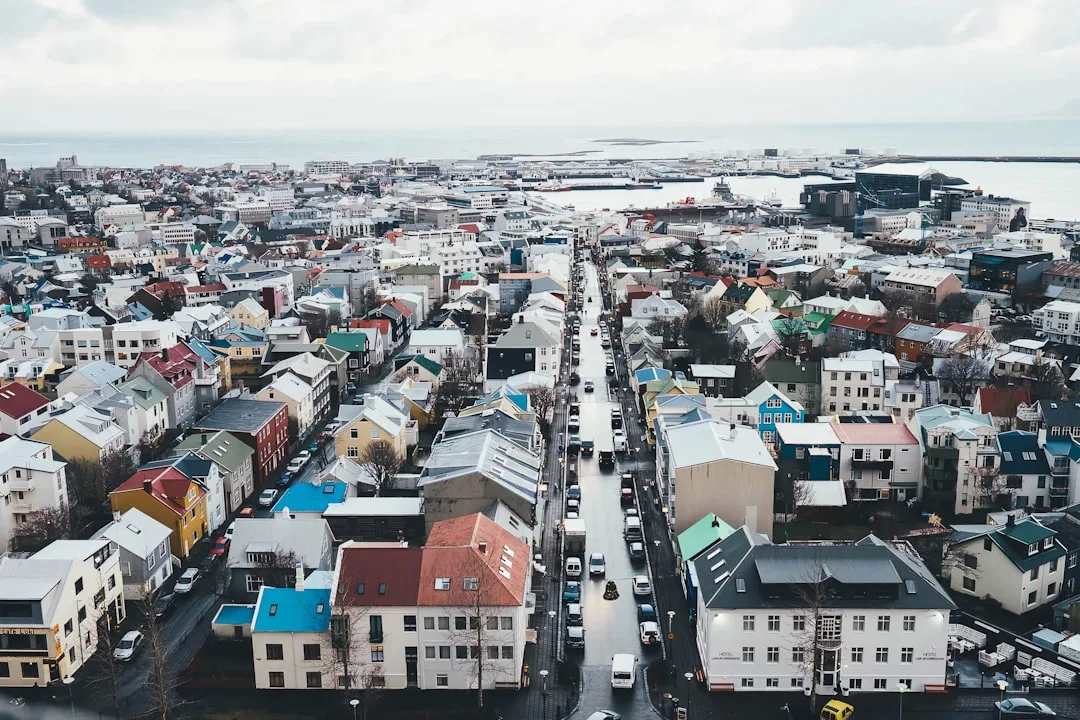 A warm illustration of Reykjavik on a clear day: the Hallgrimskirkja church tower rising above the colourful rooftops of the old harbour district, with soft mountains in the distance.