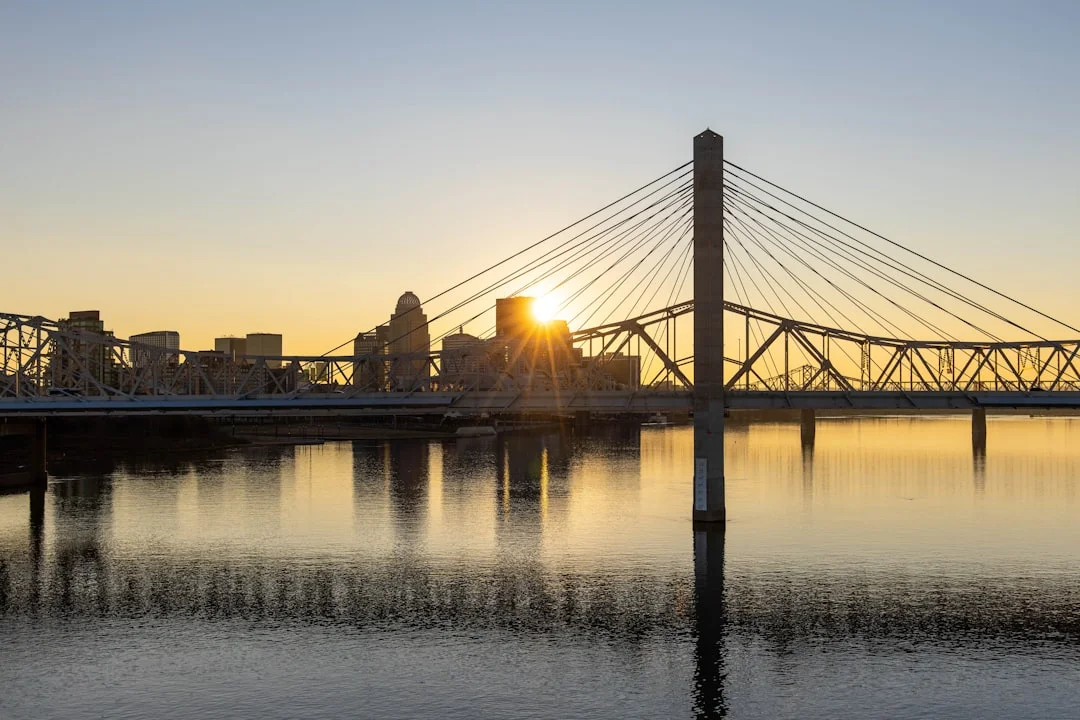 Louisville, Kentucky skyline at sunset reflected in the Ohio River, bridge and city towers in warm evening light.