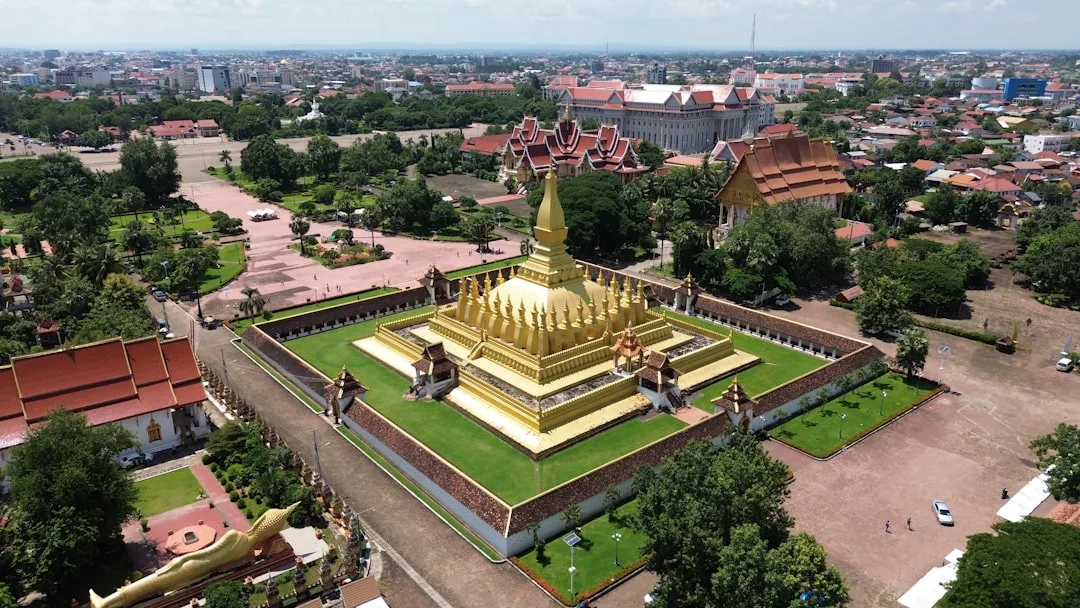 A freelance contractor in Vientiane working at a desk near a window, with the Mekong River and the That Luang temple spire visible in the warm afternoon light outside.