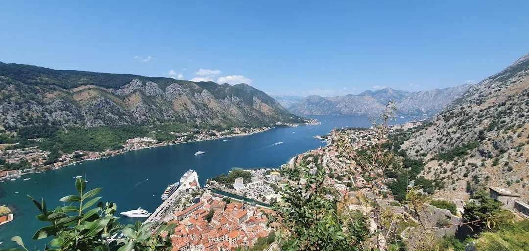 A warm illustration of Kotor on the Bay of Kotor at golden hour: the old town walls below a steep green mountain, terracotta rooftops, and calm Adriatic water in the foreground.
