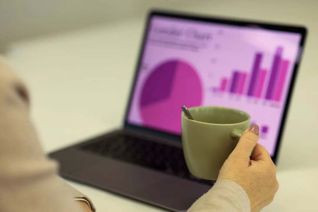 A founder reviews payroll figures on a laptop in a bright Wellington office, harbour visible through the window behind.