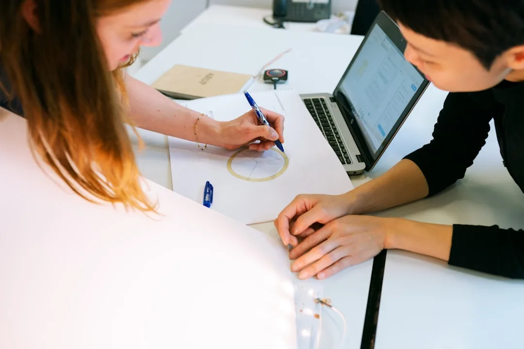Two colleagues signing a written employment agreement at a bright desk in an Auckland office, ferns visible through the window.