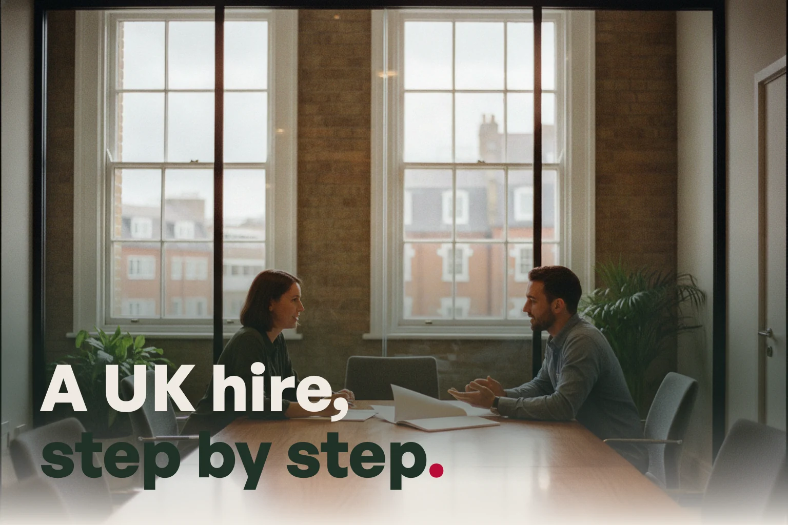 Two colleagues talking across a table in a London meeting room, with the line A UK hire, step by step.